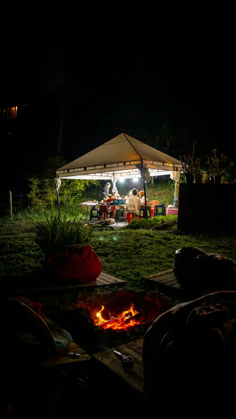 La carpa del taller encendida de noche en el jardín, con una fogata al frente