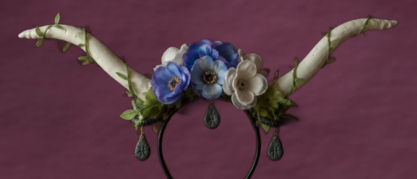 Corona de poder de porcelanicrón: dos cuernos blancos con enredadera, un ramo de flores azules y blancas, y dijes que cuelgan sobre una balaca negra