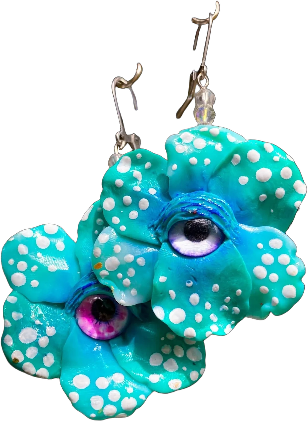Aretes de porcelanicrón: dos flores turquesa con puntos blancos, cada una con un ojo, una de iris lila y otra de iris magenta, con pestañas doradas pintadas