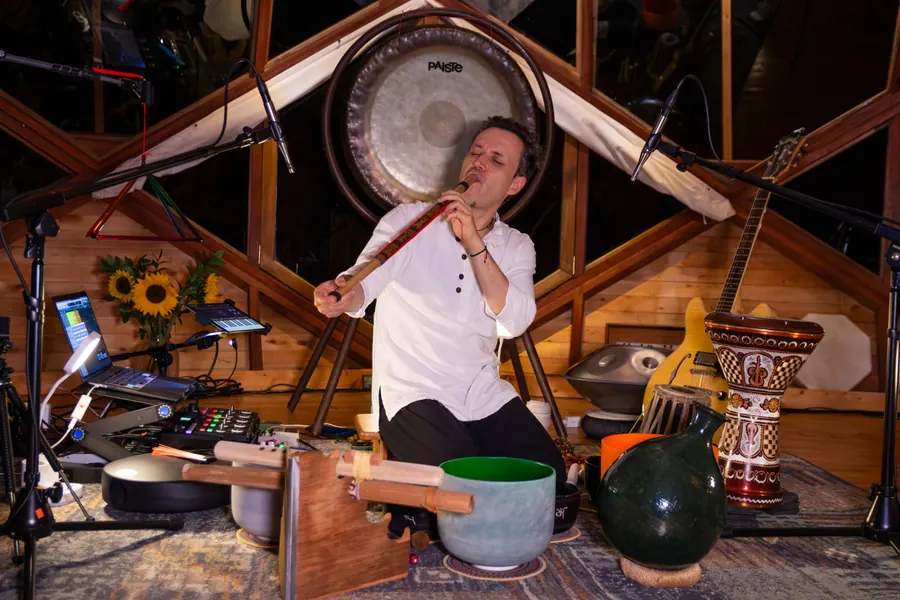 Mauro D'León toca la flauta frente a un gong, bajo el techo de madera de su estudio
